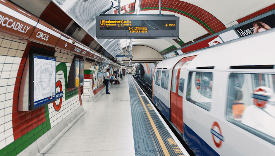 Inside East Croydon station, a modern interior features wide, tiled stairs with a red safety railing on the right side, leading up to a glass and steel upper level. To the left of the stairs, there ar