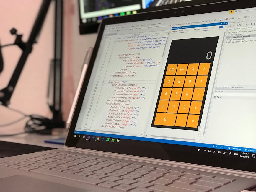 Close-up view of a laptop screen displaying lines of HTML code alongside a large digital calculator interface with orange buttons for numbers and basic operations. The laptop is situated on a desk, wi